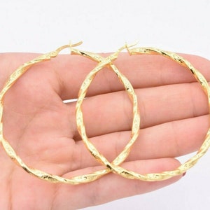 May include: A pair of gold hoop earrings with a twisted design. The earrings are large and have a shiny finish.