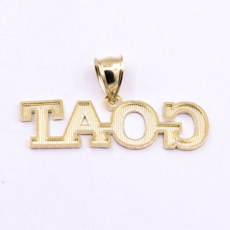May include: Gold pendant necklace with the letters "TAO" in a bold, blocky font. The pendant has a textured surface and a simple bail.