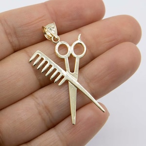Puede incluir: Encanto de colgante dorado con un par de tijeras y un peine, símbolo de la profesión de peluquería.