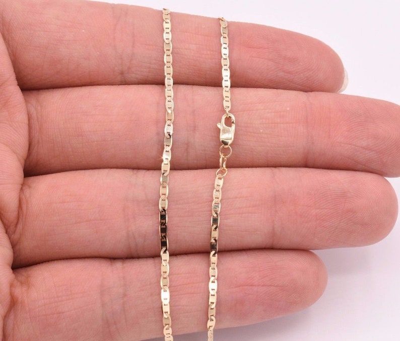 May include: A gold chain necklace with a lobster clasp. The chain is made of small, flat, oval-shaped links.