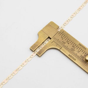Puede incluir: Primer plano de una cadena de oro medida con una regla de lat&oacute;n. La regla est&aacute; marcada en pulgadas y mil&iacute;metros. La cadena mide aproximadamente 19 pulgadas.