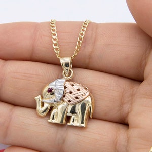 May include: A gold elephant pendant necklace with a red stone eye. The pendant is made of three different shades of gold, with a woven pattern on the back.
