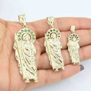 May include: Three gold pendants featuring a religious figure with a halo of green stones. The pendants are of different sizes and are displayed on a hand.