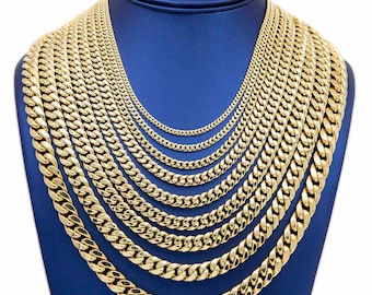 May include: A display of gold-colored Cuban link chain necklaces of varying lengths and thicknesses. The chains are arranged on a blue jewelry display, showcasing the different sizes and styles available. The links are closely interlocked, reflecting light.