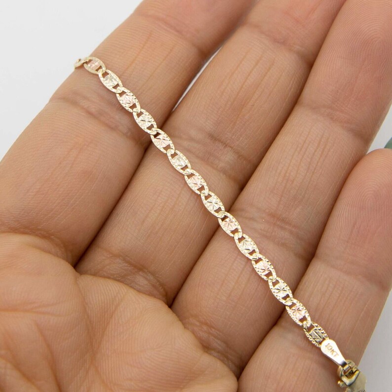 K&ouml;nnte beinhalten: Ein goldenes Kettenarmband mit einem zarten, gemusterten Design. Die Kette ist aus 10 Karat Gold gefertigt und hat einen sicheren Verschluss.