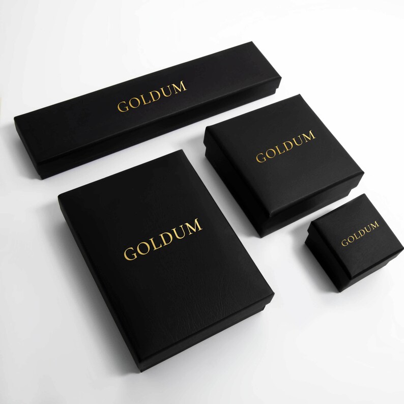 May include: Four black boxes with the word "GOLDUM" printed in gold lettering. The boxes are of different sizes, with the largest box at the top and the smallest box at the bottom.