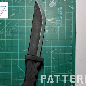 May include: A black knife with a black handle and a silver blade is placed on a green cutting mat with a white grid pattern. The mat has the text "CUTTING MAT GRID SIZE 1/17" printed on it. The word "PATTERN" is printed in white on the green mat.