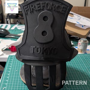 May include: Black and white 3D printed helmet with the words "FIREFORCE 8 TOKYO" on the front. The helmet has a cage-like design around the bottom.