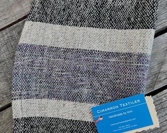 May include: A folded textile with a woven pattern in black, white, and purple hues. The design features horizontal stripes of varying widths. A blue tag with the text "CIMARRON TEXTILES Handmade by Kim" is attached.