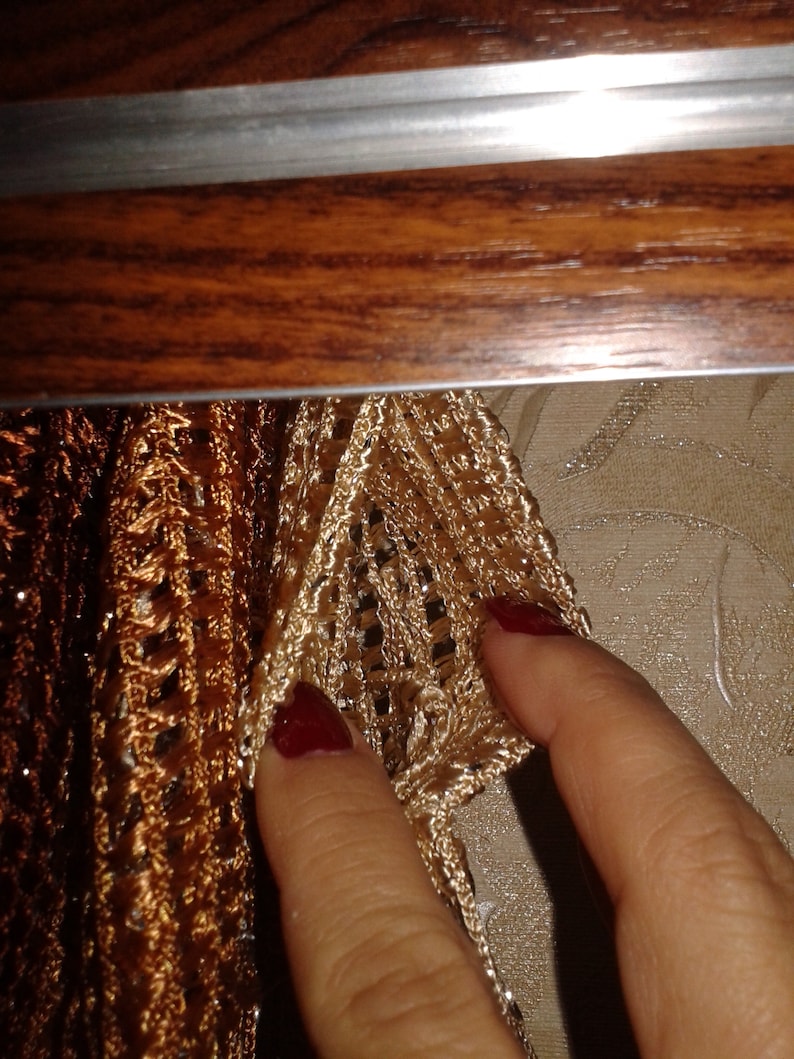May include: Close-up of a gold and brown crocheted curtain with a hand reaching out to touch it.
