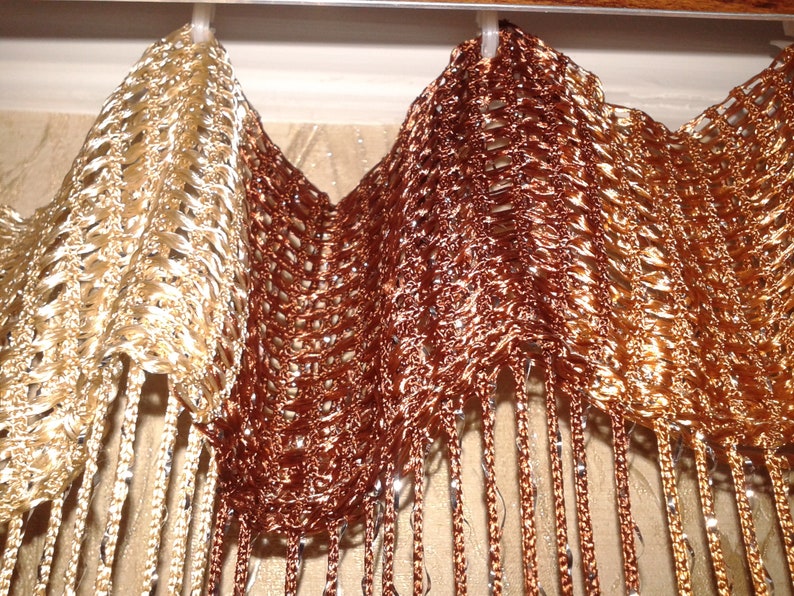 May include: A pair of gold and brown beaded curtains with a woven pattern. The curtains are hanging from a rod and have a fringe at the bottom.