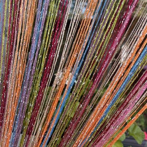 May include: Colorful string curtain with a variety of colors including orange, blue, green, and pink. The curtain has a shimmering, glittery effect, and is likely used as a decorative window treatment.