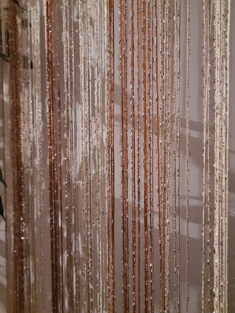 May include: A curtain made of thin, metallic strands in shades of gold and silver. The strands are woven together to create a shimmering, iridescent effect.