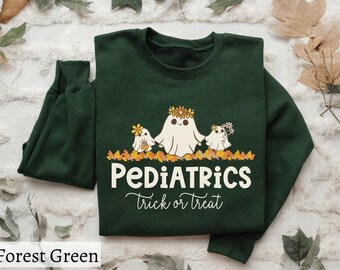 May include: A forest green crewneck sweatshirt featuring a graphic of three white ghosts wearing flower crowns, standing in a pile of autumn leaves. The text reads PEDIATRICS in a bold cream font and trick or treat in a cursive white script.