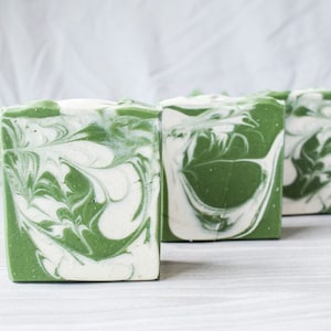 Puede incluir: Tres barras de jabón hechas a mano con un diseño marmoleado verde y blanco. El jabón está hecho con ingredientes naturales y es perfecto para pieles sensibles.