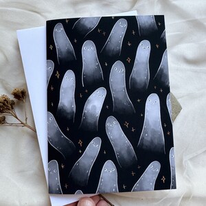 May include: A black card with a white background featuring a repeating pattern of white ghosts with smiling faces on a black background with gold stars.