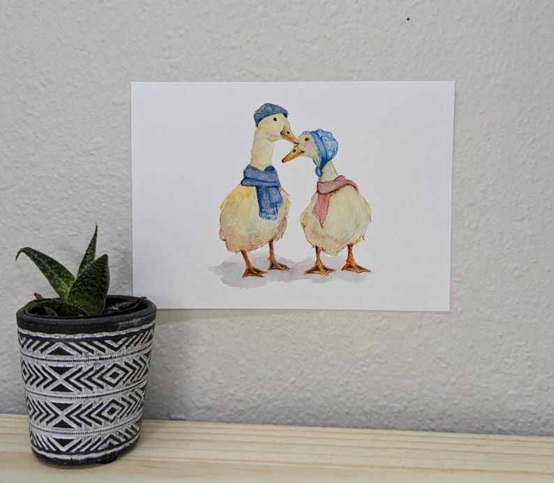 K&ouml;nnte beinhalten: Zwei Aquarell-Enten, die blaue und rosa Schals und H&uuml;te tragen. Die Enten schauen sich an und scheinen sich anzusehen.