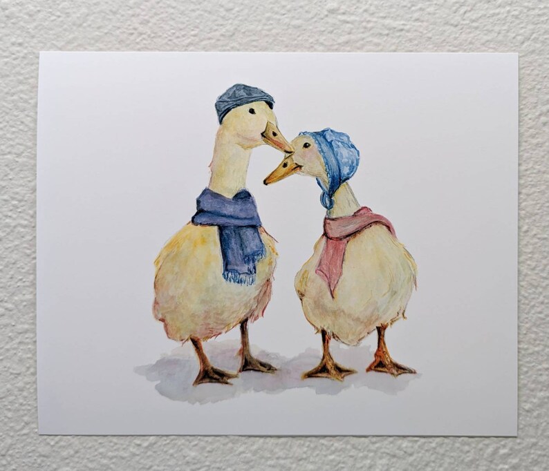 K&ouml;nnte beinhalten: Zwei Aquarell gemalte Enten, die blaue und rosa Schals und H&uuml;te tragen. Die Enten schauen sich an und scheinen sich zu k&uuml;ssen.