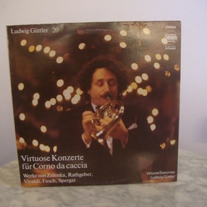 Könnte beinhalten: Vintage Schallplattenhülle mit einem Mann, der ein Blechblasinstrument spielt. Das Album trägt den Titel "Virtuose Konzerte für Corno da caccia" von Ludwig Güttler. Der Hintergrund ist ein verschwommenes, warmtoniges Bild mit Bokeh-Lichtern.