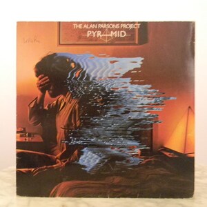 Könnte beinhalten: Albumcover für "Pyramid" von The Alan Parsons Project. Das Artwork zeigt eine Person mit verdecktem Gesicht, überlagert mit einem digitalen Verzerrungseffekt. Der Albumtitel und der Künstlername sind sichtbar.
