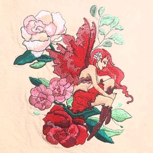 May include: Embroidered design featuring a red-winged fairy sitting on a red rose with pink and green foliage.