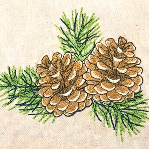 May include: Embroidered design of two brown pine cones with green pine needles on a beige fabric background.