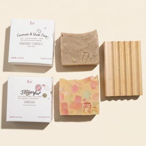 May include: Two white rectangular soap boxes labeled Coconuts & Quiet Time and Flowerful, two square soap bars with the Fiz logo, and a rectangular wooden soap dish with vertical ridges. The soap bars are beige and multicolored mosaic.