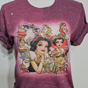 May include: A maroon t-shirt with a faded graphic print of Snow White and the Seven Dwarfs. The print features Snow White with a deer, the Evil Queen, and the dwarfs.