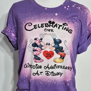 May include: Purple t-shirt with a bleach-splattered design featuring Mickey and Minnie Mouse kissing. The text reads "Celebrating Our 24th Wedding Anniversary At Disney".