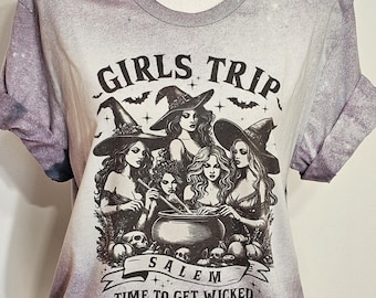 May include: A purple tie-dye t-shirt with a black and white graphic of four witches stirring a cauldron. The graphic includes the text "Girls Trip Salem Time to Get Wicked".