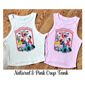 May include: Two crop tank tops with the text "Easy-Bake Coven" and a graphic of three girls baking. One tank top is natural and the other is pink.