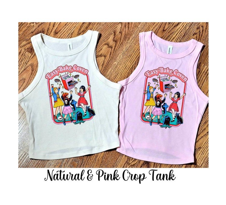 May include: Two crop tank tops with the text "Easy-Bake Coven" and a graphic of three girls baking. One tank top is natural and the other is pink.