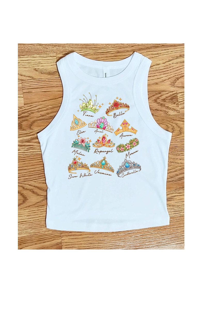 Peut inclure: D&eacute;bardeur blanc avec des illustrations color&eacute;es de diad&egrave;mes de princesses. Chaque diad&egrave;me est &eacute;tiquet&eacute; avec le nom d'une princesse, notamment Tiana, Belle, Elsa, Ariel, Aurora, Mulan, Raiponce, Moana, Blanche-Neige, Jasmine et Cendrillon.