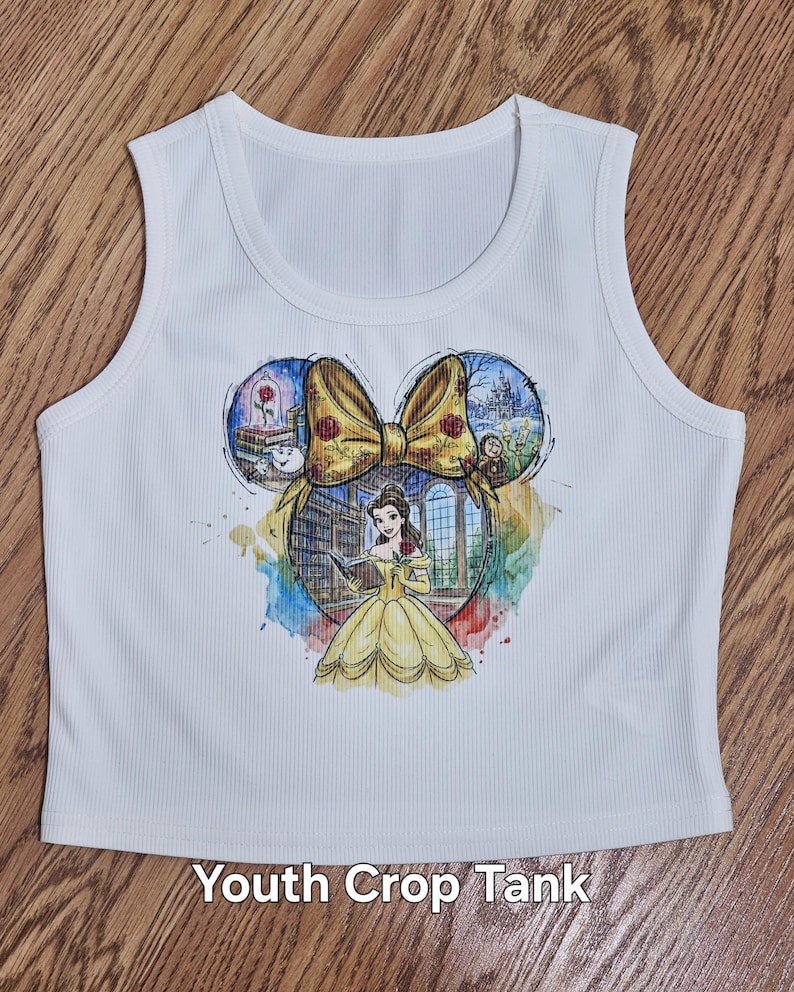 Peut inclure: D&eacute;bardeur court blanc pour jeunes avec un motif color&eacute; de Belle de La Belle et la B&ecirc;te, un n&oelig;ud jaune et des illustrations du ch&acirc;teau et de la rose. Le texte "Youth Crop Tank" est imprim&eacute; en bas.