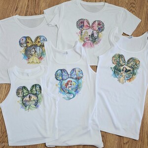 Peut inclure: Cinq t-shirts et d&eacute;bardeurs blancs avec des motifs color&eacute;s de princesses Disney. Chaque v&ecirc;tement pr&eacute;sente une forme de t&ecirc;te de Mickey Mouse avec une image de princesse &agrave; l'int&eacute;rieur. Les princesses incluent Belle, Ariel, Tiana, Pocahontas et Aurora.