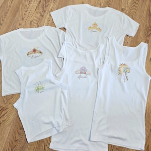 Peut inclure: T-shirts et d&eacute;bardeurs blancs avec des motifs de couronnes color&eacute;es et des noms. Les chemises pr&eacute;sentent des couronnes avec des noms comme Bella, Ariel et Aurora. Les d&eacute;bardeurs ont un design sans manches.