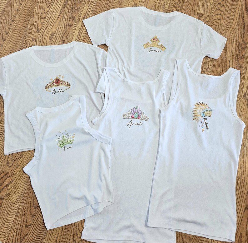 Peut inclure: T-shirts et d&eacute;bardeurs blancs avec des motifs de couronnes color&eacute;es et des noms. Les chemises pr&eacute;sentent des couronnes avec des noms comme Bella, Ariel et Aurora. Les d&eacute;bardeurs ont un design sans manches.