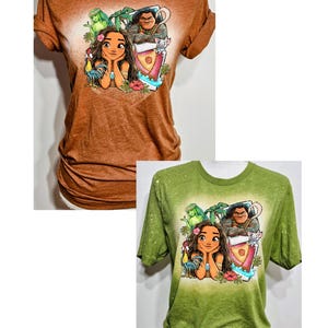 May include: Two t-shirts featuring a cartoon character from the film Moana. The shirt on the left is burnt orange and the shirt on the right is leaf green. Both shirts state "Adult Only".
