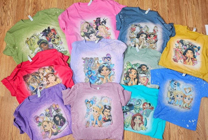 May include: A collection of ten t-shirts featuring various Disney princesses and characters. The shirts are all white with a bleached design and feature characters like Cinderella, Snow White, Ariel, and Jasmine.