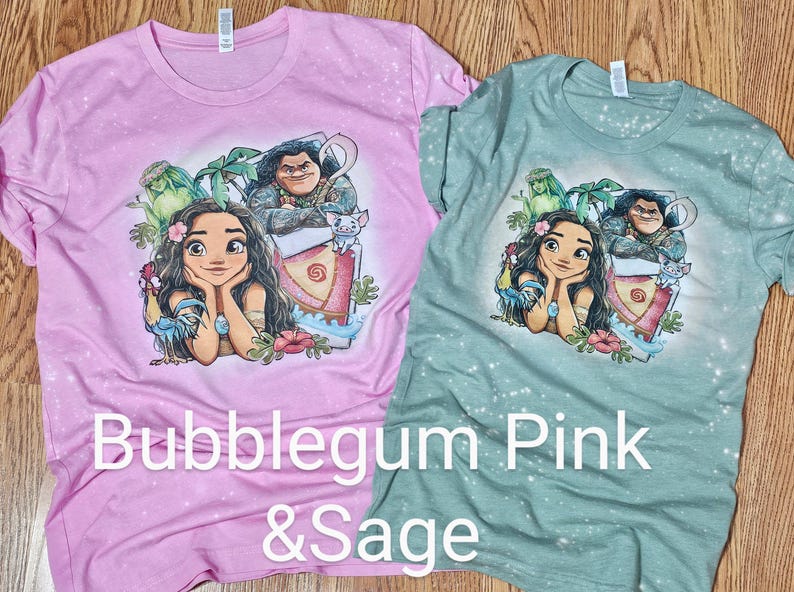 May include: Two t-shirts with a tie-dye effect. The pink shirt features a cartoon image of Moana and Maui from the Disney movie Moana. The green shirt features a cartoon image of Moana and Maui from the Disney movie Moana. The text "Bubblegum Pink & Sage" is printed on the bottom of the shirts.