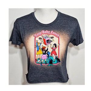 May include: A dark gray cropped t-shirt with a bleached effect. The shirt features a graphic of three girls in front of an Easy-Bake Oven with the text "Easy-Bake Coven".