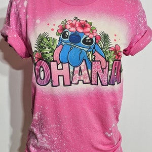 May include: Pink t-shirt with a bleach-splattered design featuring Stitch from Lilo & Stitch wearing a flower crown and the word "Ohana" in colorful letters.