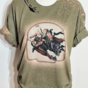 Puede incluir: Camiseta verde con efecto blanqueado y un estampado gr&aacute;fico de tres brujas volando en una escoba. El texto "Come, we fly" est&aacute; escrito sobre el gr&aacute;fico.