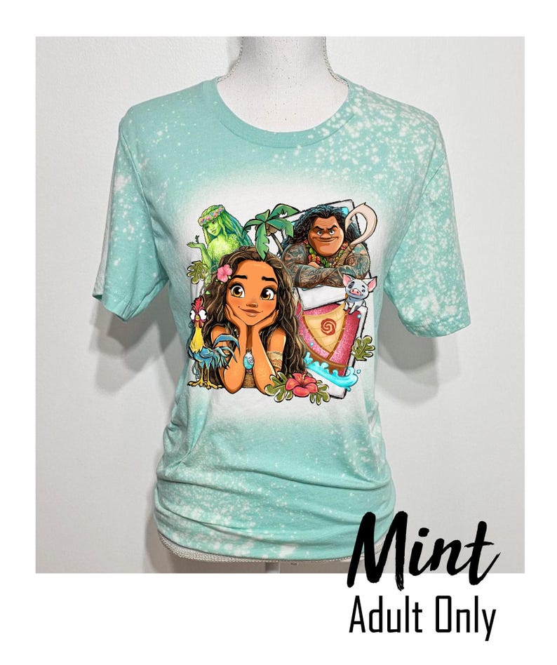 May include: A mint green t-shirt with a bleach-splattered design featuring a cartoon image of Moana, Maui, Pua, and Hei Hei from the Disney movie Moana. The text "Mint Adult Only" is printed below the image.