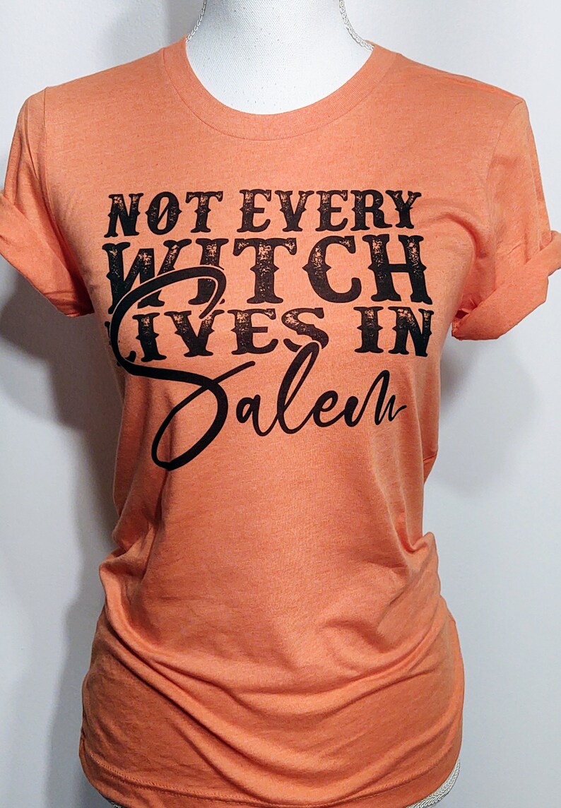 May include: Orange t-shirt with black text that reads "Not Every Witch Lives in Salem".