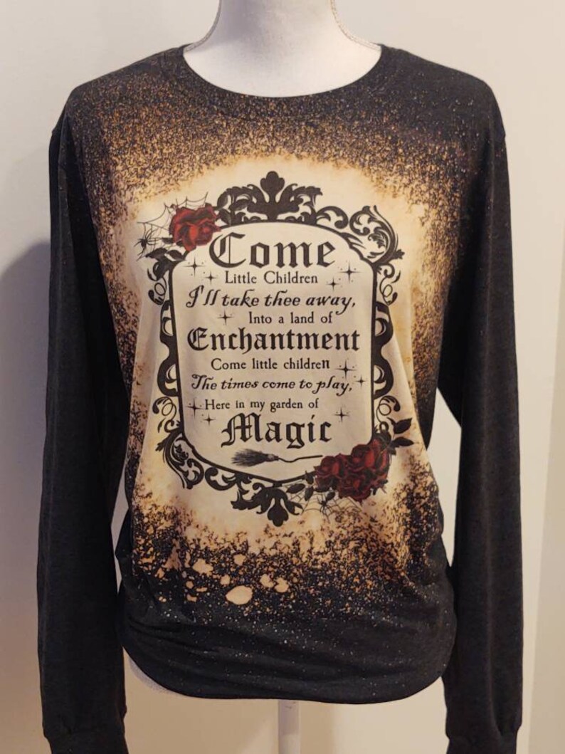 Puede incluir: Camiseta negra de manga larga con un dise&ntilde;o salpicado de lej&iacute;a que presenta una ilustraci&oacute;n de estilo vintage de un cartel enmarcado que dice "Come Little Children I'll take thee away, Into a land of Enchantment Come little children The times come to play, Here in my garden of Magic".