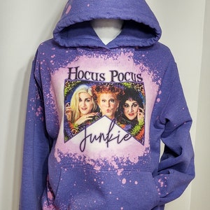 May include: Purple hooded sweatshirt with a bleach-splattered design featuring a picture of the Sanderson sisters from the movie Hocus Pocus and the text "Hocus Pocus Junkie".