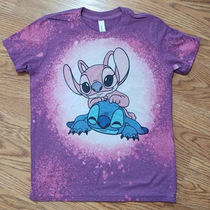 May include: Purple tie-dye t-shirt with a white graphic of Stitch and Angel from the Disney movie Lilo & Stitch.