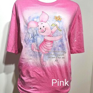 May include: A pink bleached t-shirt featuring a graphic of Piglet holding a yellow flower. The text reads Piglet and I wish you everything you wish for yourself because I love you. XO. The shirt has a faded pink color with white bleached spots.