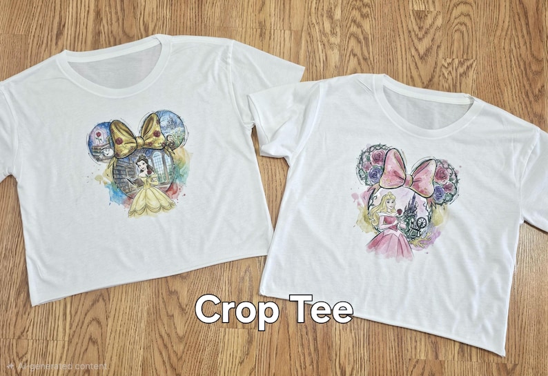 Peut inclure: Deux t-shirts courts blancs avec des motifs sur le th&egrave;me des princesses Disney. L'un repr&eacute;sente Belle, l'autre Aurore, dans une silhouette d'oreille de Mickey Mouse. Le texte "Crop Tee" est affich&eacute; en dessous.